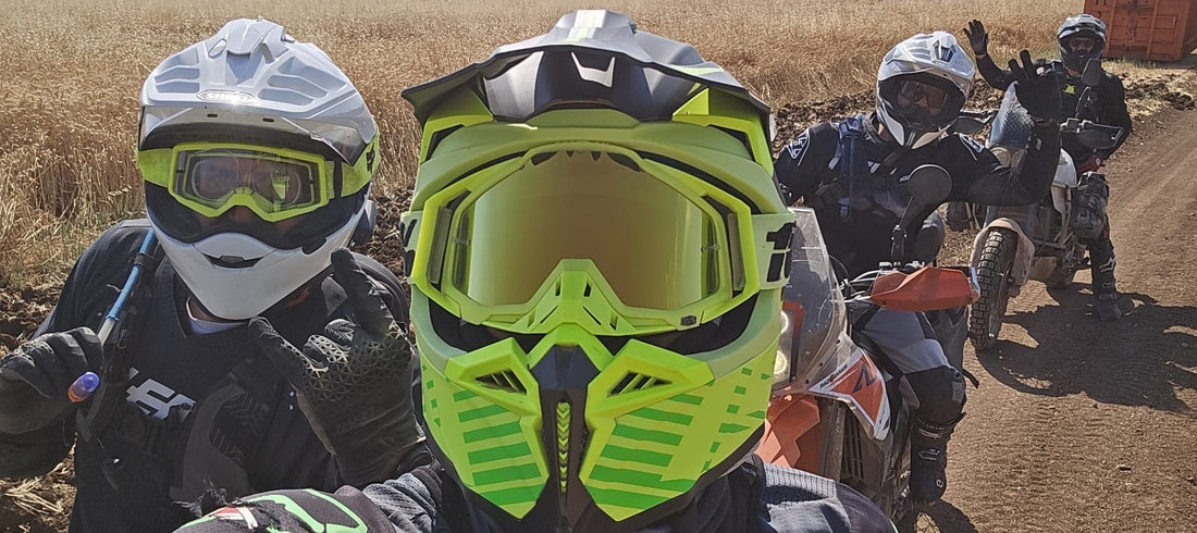 David in a green helmet with three riding friends and their KTM adventure bikes stopped on a dirt track through a wheat field